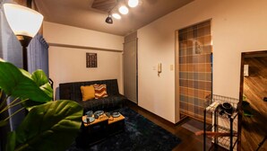Una sala de estar acogedora con un sofá, una mesa de centro y una planta. Hay una puerta corredera y un estante pequeño con objetos.