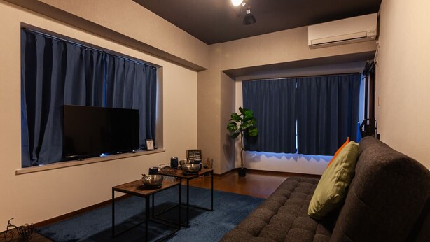 Una sala de estar con televisor de pantalla plana, un sofá, una mesa de centro y una planta grande.