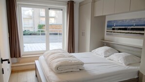 Een hotelkamer met een groot bed, een raam met gordijnen, een schilderij boven het bed en een uitzicht op het balkon.