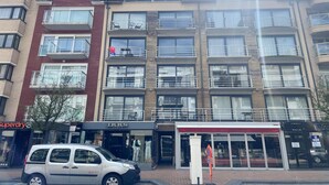Een meerlaags gebouw met balkons, winkels en een geparkeerde auto.