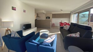 Un salon moderne comprenant un canapé, un téléviseur et un coin repas avec une table et des chaises.