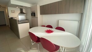 Une cuisine moderne dotée d’un îlot central, d’un coin repas avec une table blanche et des chaises rouges, et d’un îlot de cuisine intégrant un four.
