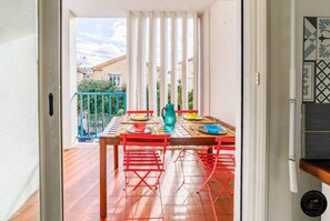 En balkon med et spisebord, blåt gelænder og udsigt til bygninger i baggrunden.