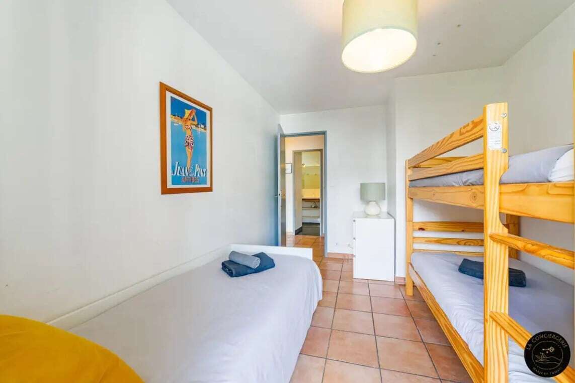 A room with a bunk bed, a single bed, a desk with a lamp, and a poster on the wall.