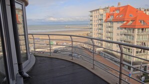 Een balkon met uitzicht op een strand, een pier en aangrenzende gebouwen.