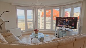 Een woonkamer met een groot raam, een bank, een glazen salontafel en een televisie.