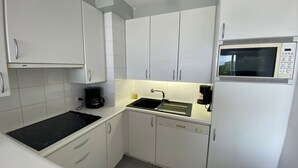 Une cuisine de taille réduite avec des meubles blancs, une cuisinière noire, un four à micro-ondes et une machine à café.