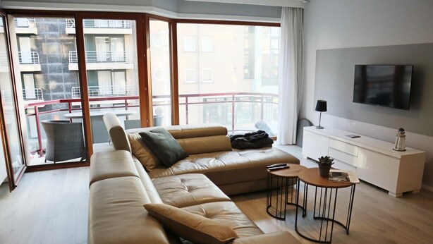 A modern living room with a large sectional sofa, a small round table, and a flat-screen TV mounted on the wall. - Apartment in Nieuwpoort near the Beach (Nieuwpoort)