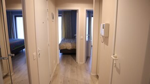 A hotel corridor with wooden flooring, a bed with a patterned bedspread, and a telephone on the wall. - Apartment in Nieuwpoort near the Beach (Nieuwpoort)