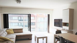 Un salon moderne comprenant un canapé, une table basse, une table à manger avec des chaises, un téléviseur et un meuble.