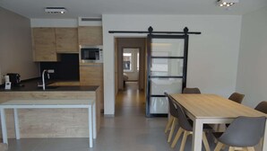 Une cuisine moderne avec un plan de travail blanc, un four à micro-ondes encastré et une machine à café. On y trouve également un coin repas avec une table et des chaises en bois.