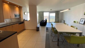 A modern kitchen with a microwave, sink, and cabinets. There is a dining area with a table and chairs, and a view of the outdoors through large windows.