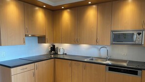 A modern kitchen with wooden cabinets, a black countertop, a built-in microwave, a coffee maker, and a dishwasher.