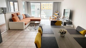 A modern living room with a sofa, dining table, and chairs. There is a TV and a window with curtains. - Apartment in Nieuwpoort near the Beach (Nieuwpoort)