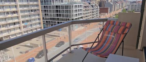 A balcony with a striped chair and a small table, overlooking a parking lot and buildings.