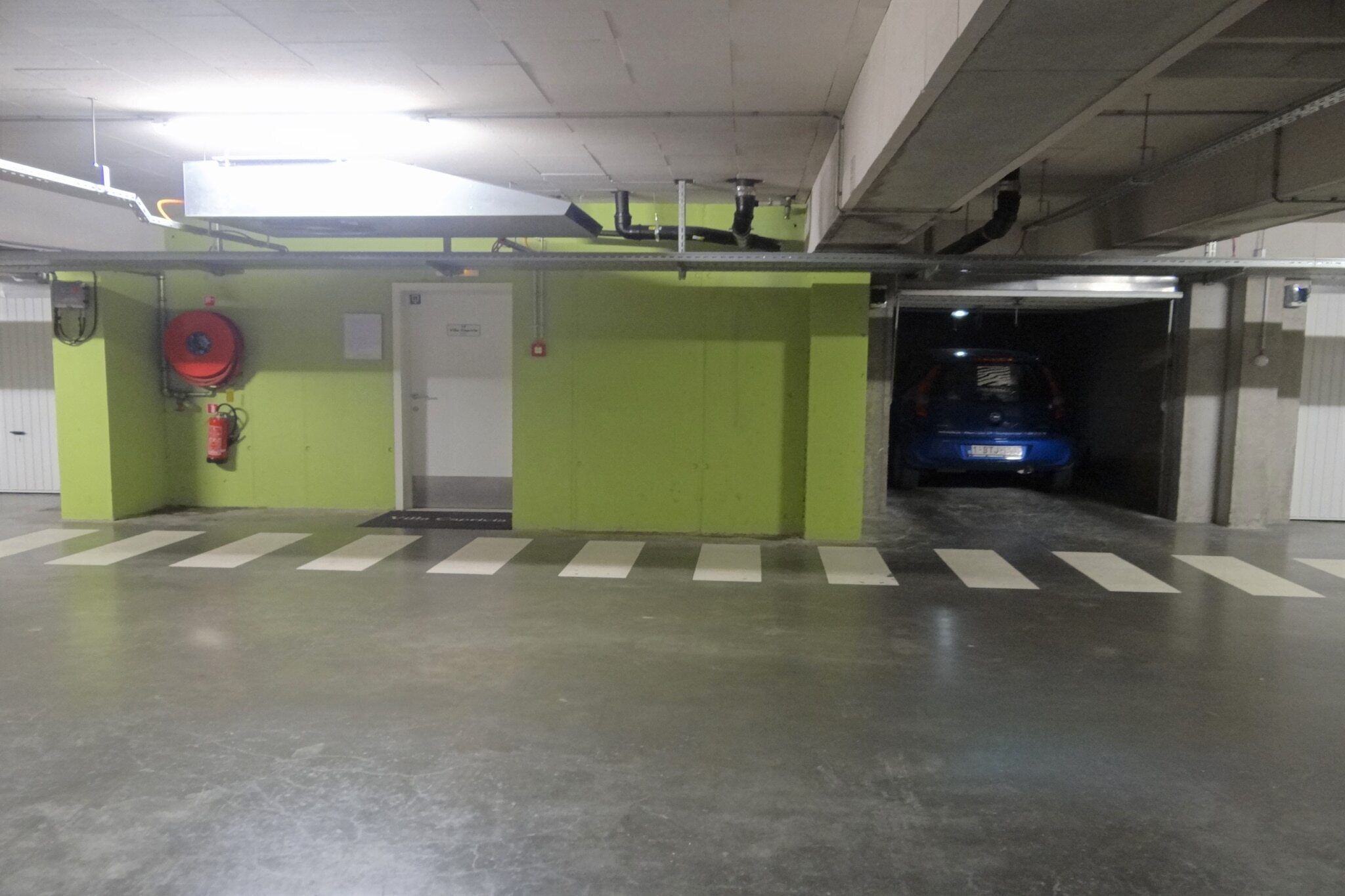 Garagem de estacionamento com paredes verdes, um extintor de incêndio e um veículo azul a entrar.