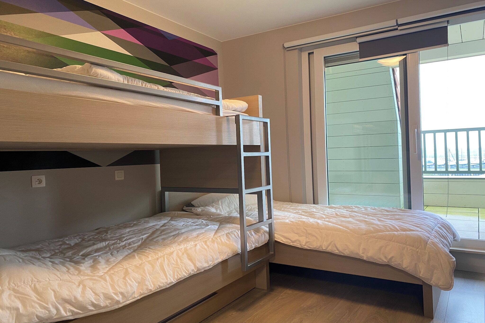 A room with two bunk beds, a window with a view, and a colorful geometric wall design.