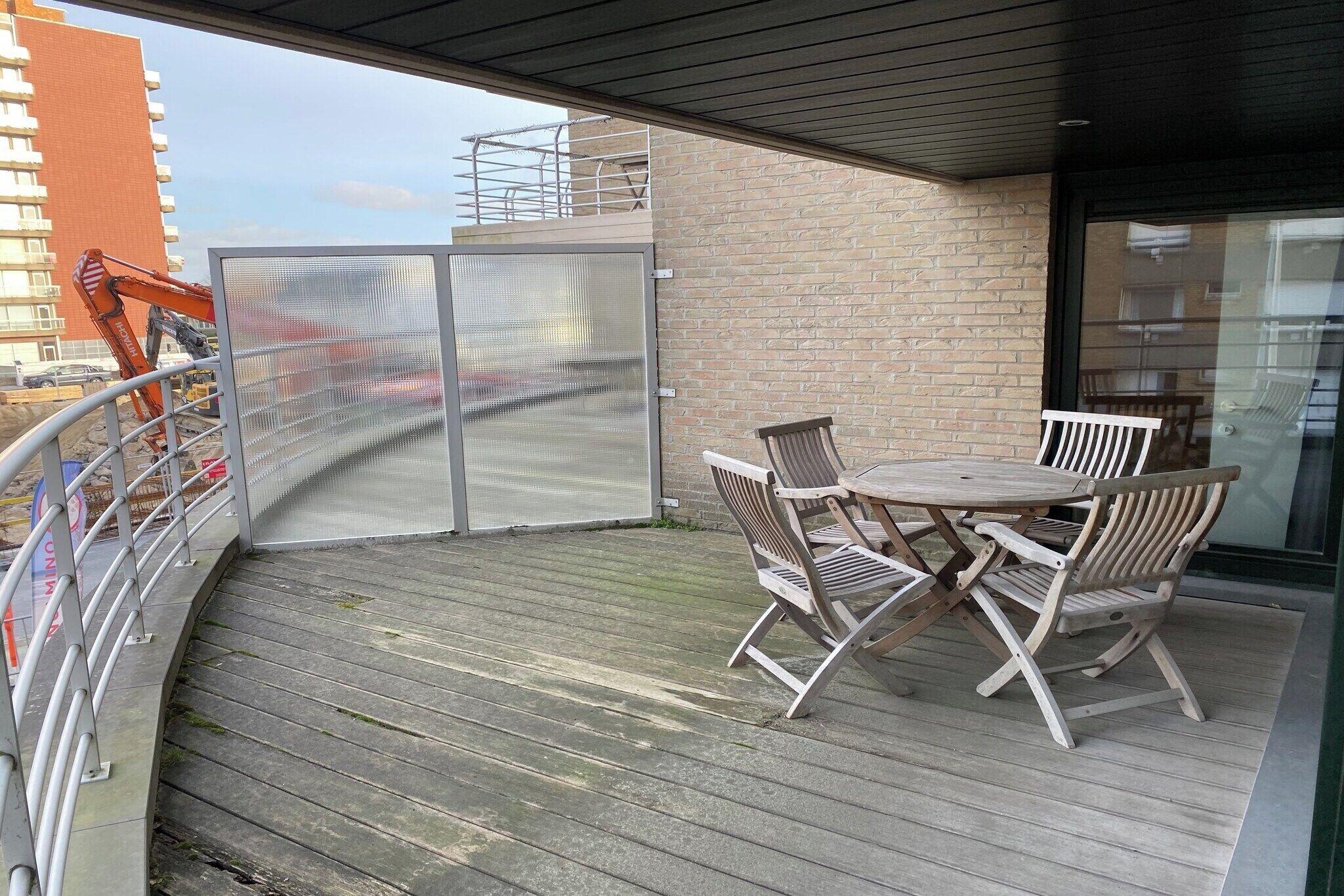 A balcony with a wooden table and chairs, a glass door, and a view of a construction site.