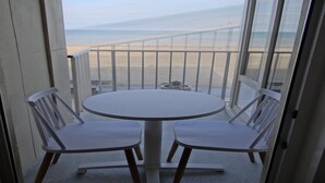 Un balcon avec une table ronde et deux chaises, donnant sur une plage et une clôture.
