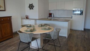 A modern kitchen with white cabinets, a central island with seating, and a decorative ship's wheel on the wall.