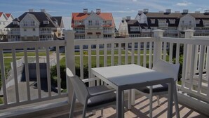 A balcony with a white table and chair, overlooking a row of houses with red roofs.