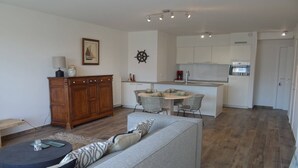 A modern living room with a grey sofa, a wooden cabinet, and a dining area with a round table and chairs.