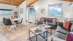 Ein gemütliches Wohnzimmer mit Holzboden, einem grauen Sofa, einem Couchtisch und einem Essbereich mit Stühlen und Tisch.