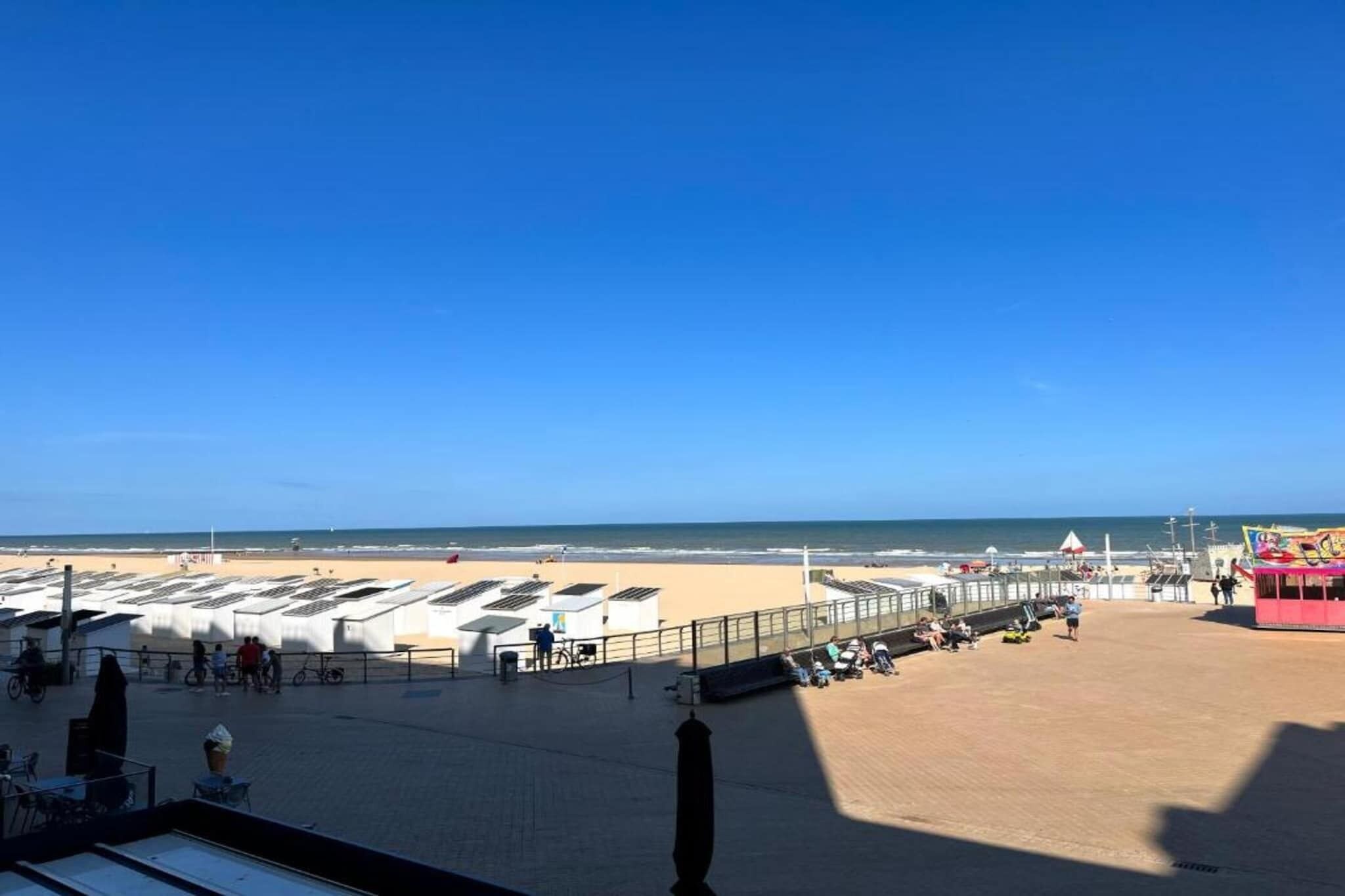 Uma praia com espreguiçadeiras, um calçadão e um edifício cor-de-rosa.