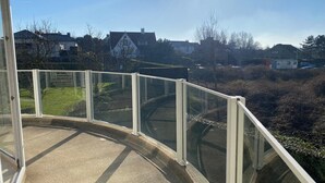 A balcony with a glass railing overlooking a residential area with houses and a clear sky. - Apartment in Nieuwpoort near the Sea Wall (Nieuwpoort)