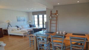 A spacious living area with a wooden dining table, blue chairs, a sofa, and a ladder against the wall. - Bright Attic with Sea Breeze (Nieuwpoort)