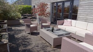 An outdoor patio with wicker furniture, a white sofa, and a glass table. - Bright Attic with Sea Breeze (Nieuwpoort)
