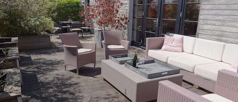 An outdoor patio with wicker furniture, a white sofa, and a glass table.
