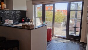 A modern kitchen with a large window, a counter with kitchen appliances, and a red trash bin. - Bright Attic with Sea Breeze (Nieuwpoort)