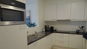 A modern kitchen with white cabinets, a stainless steel oven, a sink, and a coffee maker.