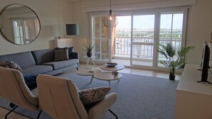 A modern living room with a grey sofa, two armchairs, a coffee table, and a large window with a view of a marina.