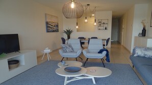 A modern living room with a TV, seating area, dining space, and a hallway.