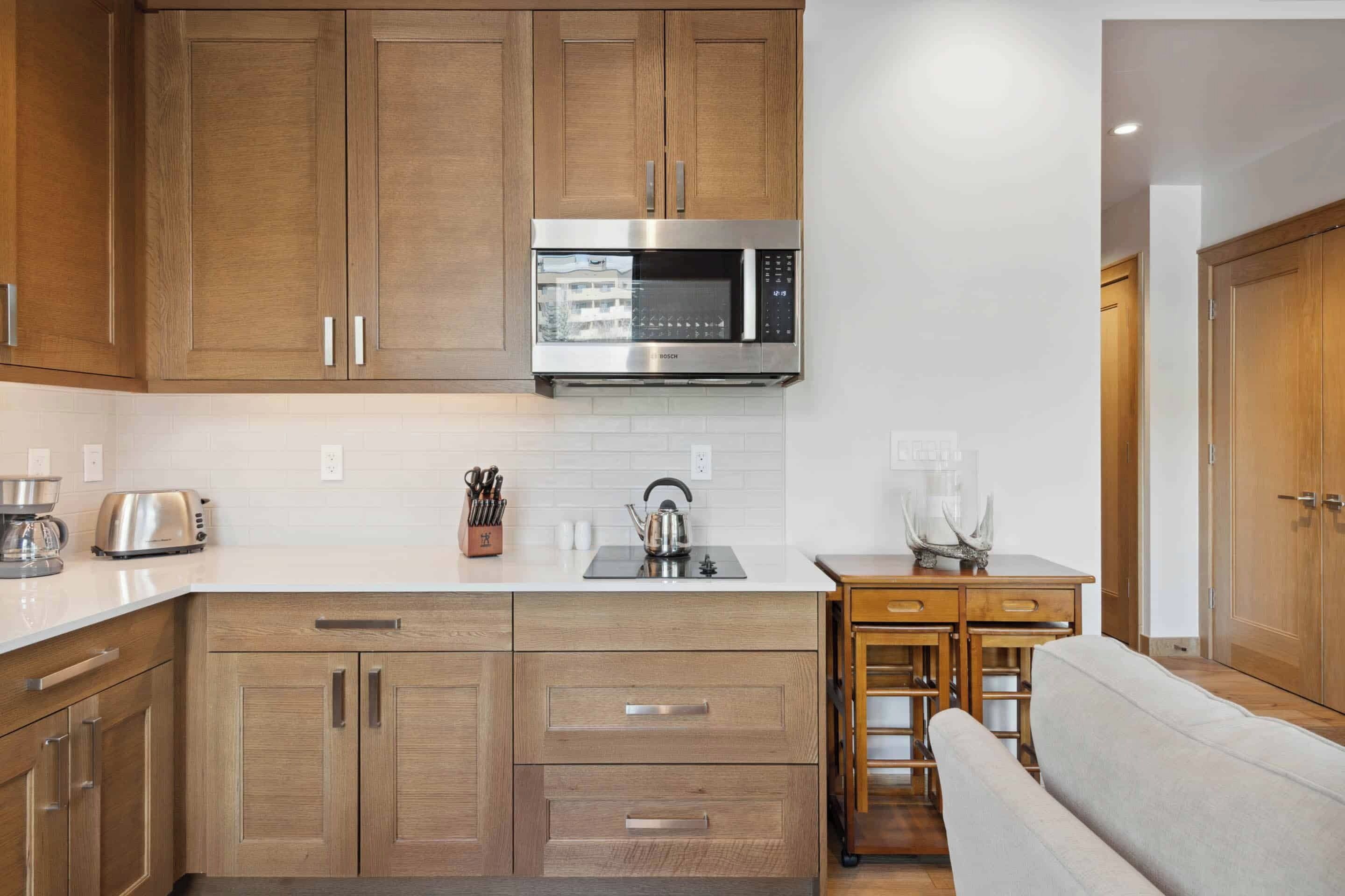 A modern kitchen with wooden cabinets, a stainless steel Bosch microwave, a white countertop, and a built-in sink.