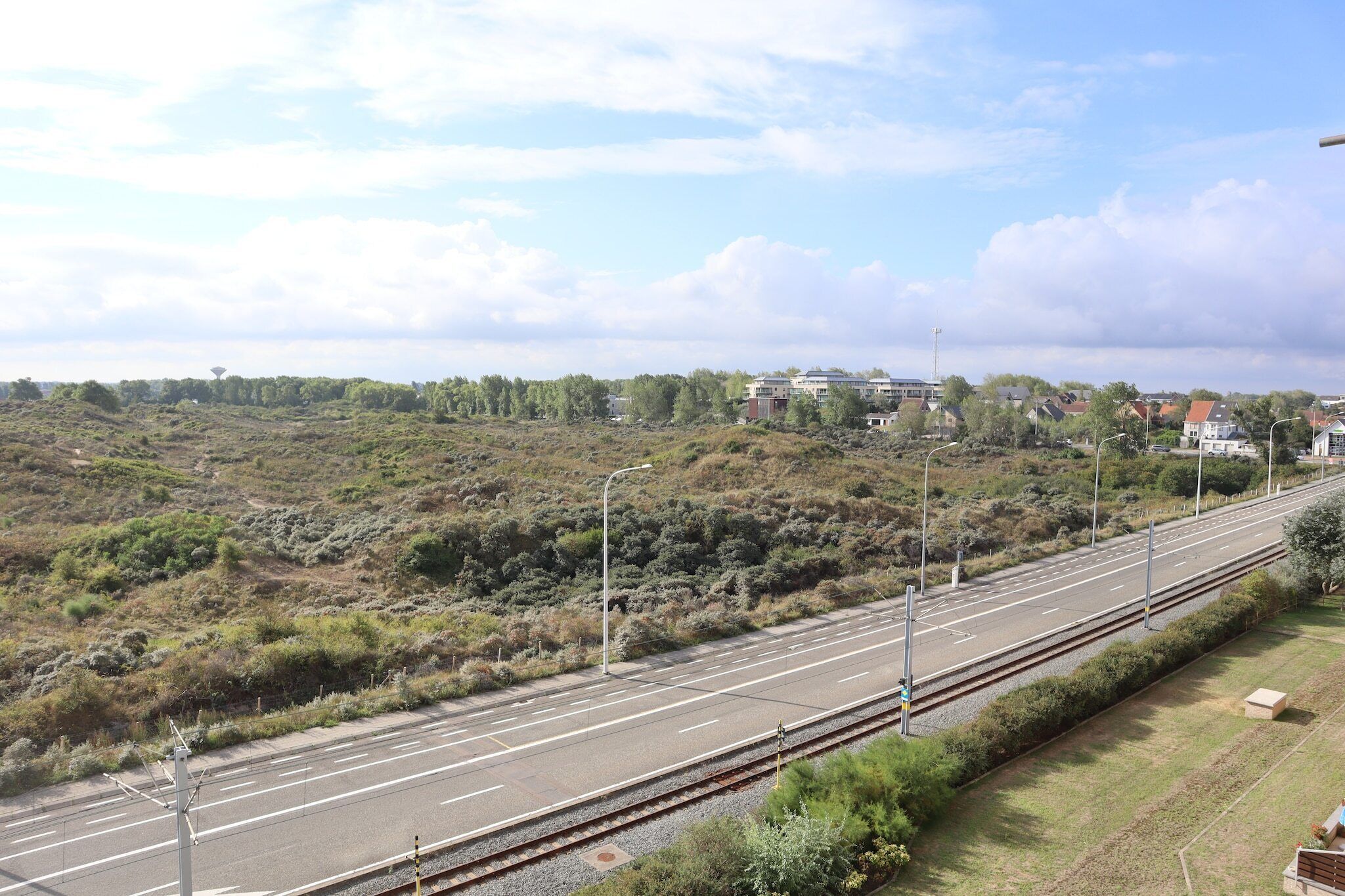 A highway with multiple lanes, adjacent to a railway track, surrounded by greenery and residential buildings.
