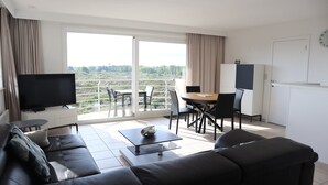 Ein modernes Wohnzimmer mit Sofa, Couchtisch, Fernseher und einem Balkon mit Essbereich.