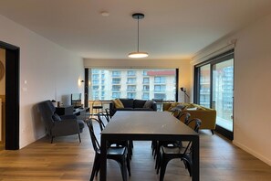 Enjoy a spacious living area with a large dining table and comfortable seating, offering a view of the city.