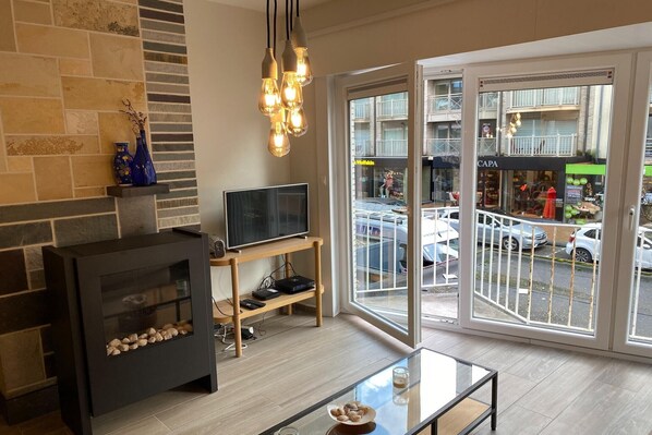 Ein modernes Wohnzimmer mit Kamin, Fernseher und großen Fenstern mit Blick auf eine Straße.