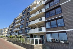 Un immeuble résidentiel à plusieurs étages, doté de balcons et d’une façade en briques, avec un ciel dégagé.