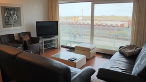 A modern living room with a large window, a flat-screen TV, and comfortable seating.