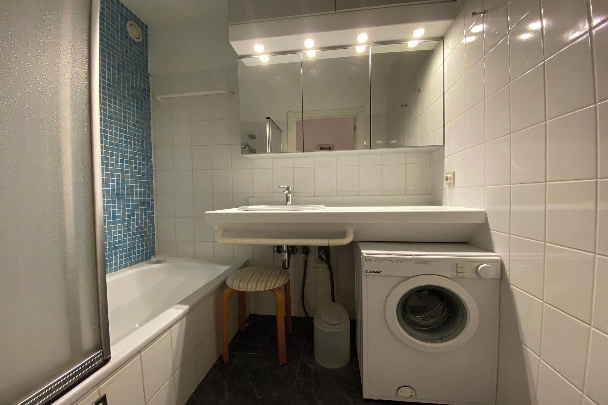 Un baño pequeño con lavamanos, espejo y lavadora.