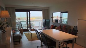Una sala de estar moderna con comedor, televisor y vista al mar.