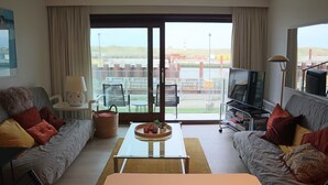 Habitación de hotel moderna con sofá, una mesita de café, televisión y vistas a una zona industrial a través de amplios ventanales.