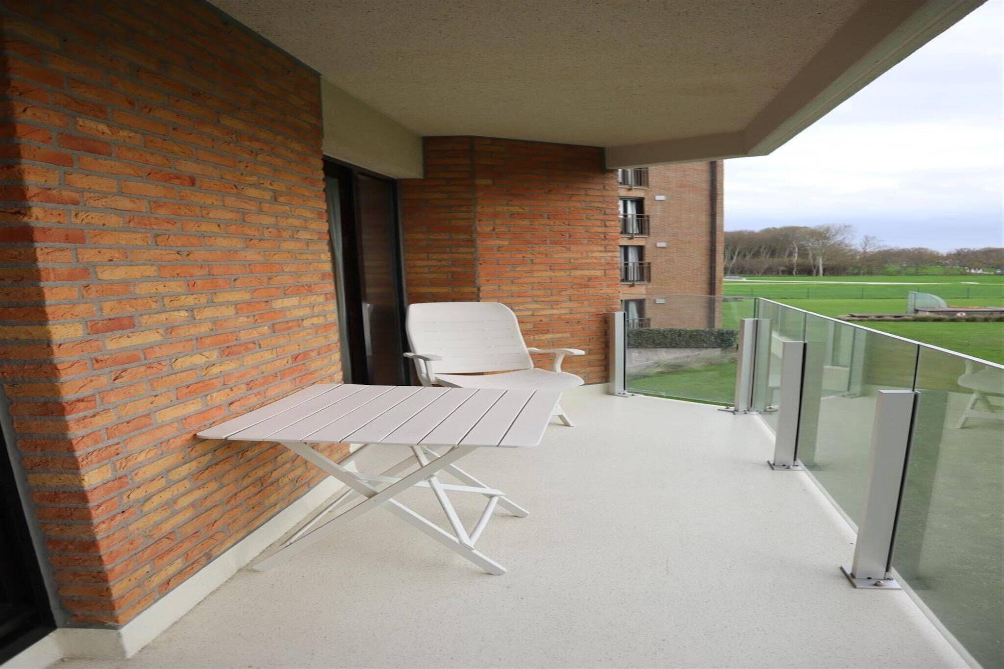 A balcony with two white chairs and a table, brick walls, and a view of a green field.