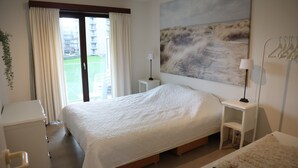 Habitación de hotel con una cama grande, un escritorio, una silla, una mesita de noche pequeña con lámpara y un ventanal con cortinas.