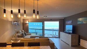 Een moderne woonkamer met een bank, eettafel en televisie. Een groot raam biedt uitzicht op de oceaan en een pier.