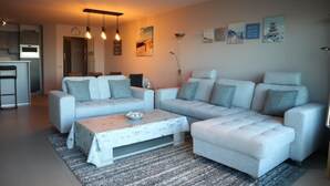 Een moderne woonkamer met een hoekbank, een salontafel en een keuken op de achtergrond.